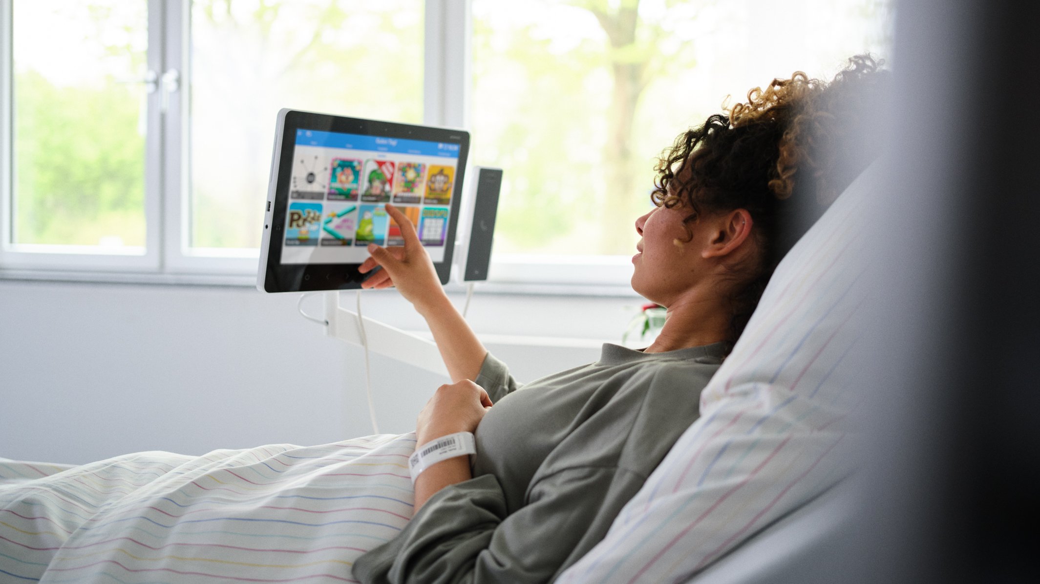 BEWATEC Patientenentertainment | Patientin liegt im Bett und spielt etwas auf Bedside Terminal