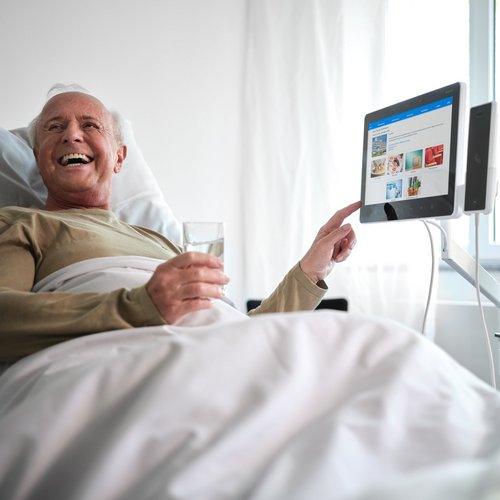 BEWATEC Patientenentertainment | Patient bedient lachend das Bedside Terminal