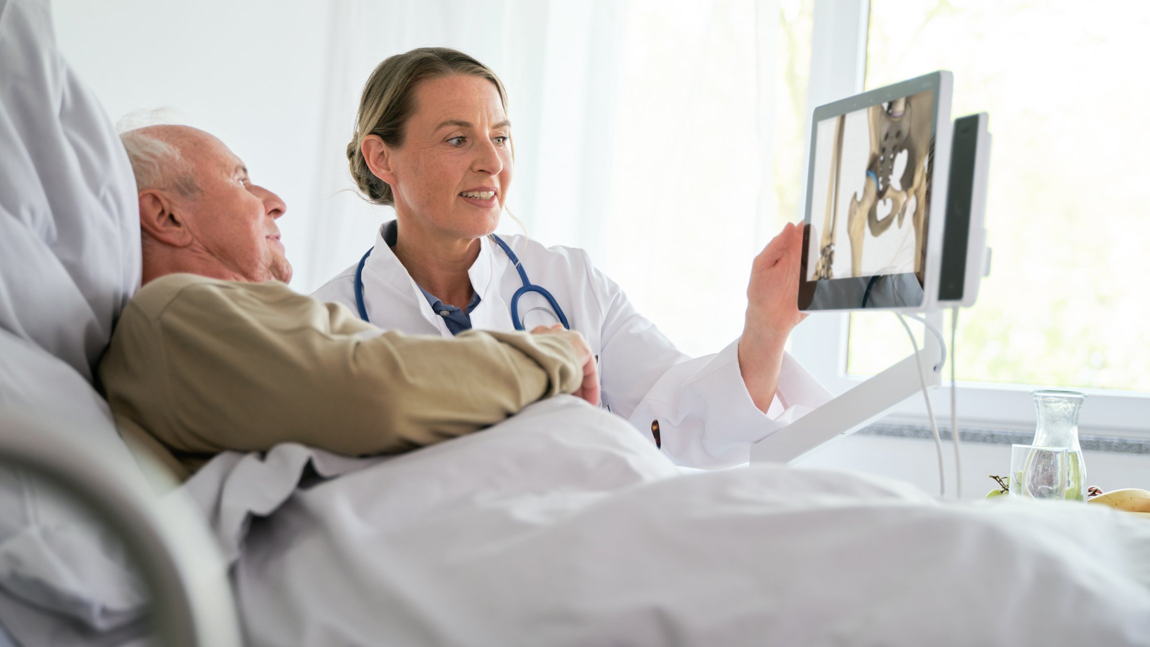BEWATEC Patienten informieren | Ärztin zeigt Patient im Bett Röntgenaufnahmen auf Bedside Terminal