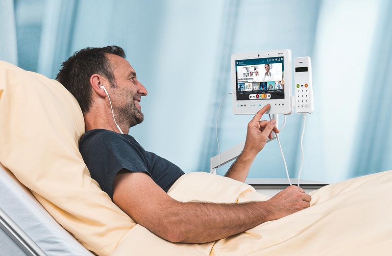 BEWATEC Unternehmensgeschichte | Patient im Krankenhausbett bedient BEWATEC Tablet MediPaD